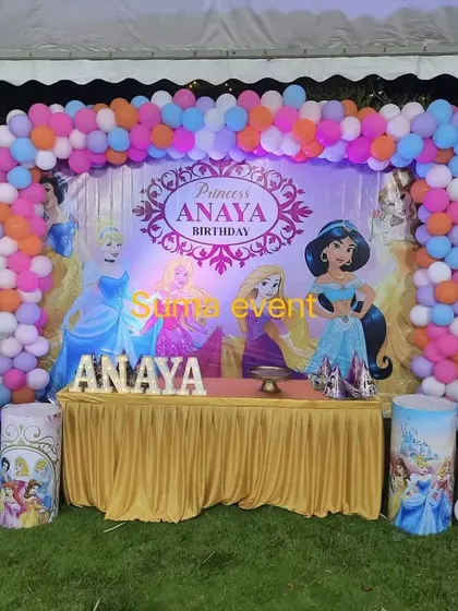 An outdoor Disney Princess party for Anaya. The decoration includes a large backdrop with Cinderella, Jasmine, and Rapunzel, framed by a colorful balloon arch that stands out beautifully on the lawn.