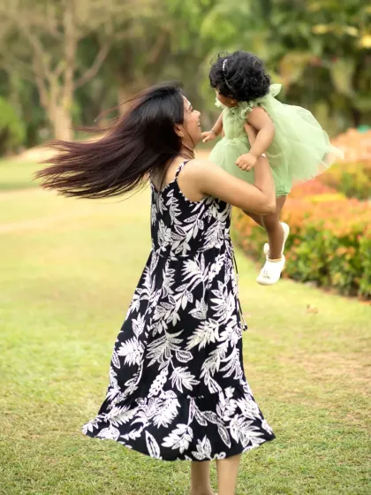 A mother joyfully twirls in a park with her daughter held high in her arms, her hair flying in a beautiful display of motion and happiness.