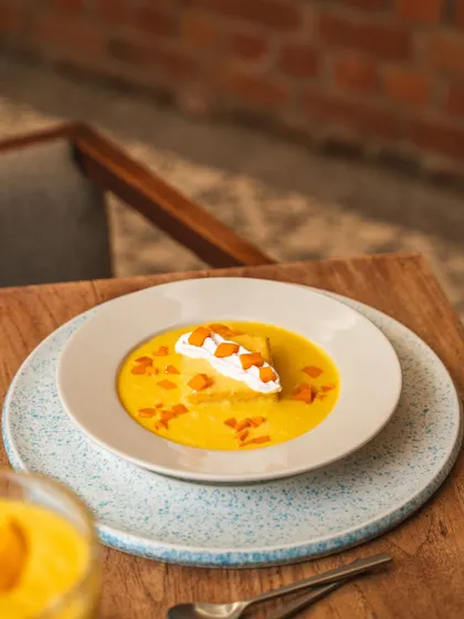 A bright and cheerful mango soup dessert, shot outdoors on a wooden table. The natural light brings out the vibrant yellow color, making it look fresh and summery.