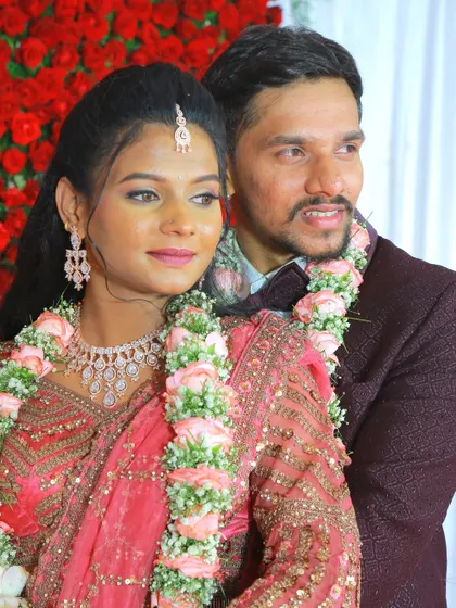 A lovely portrait of a couple adorned with pink rose garlands at their wedding event.