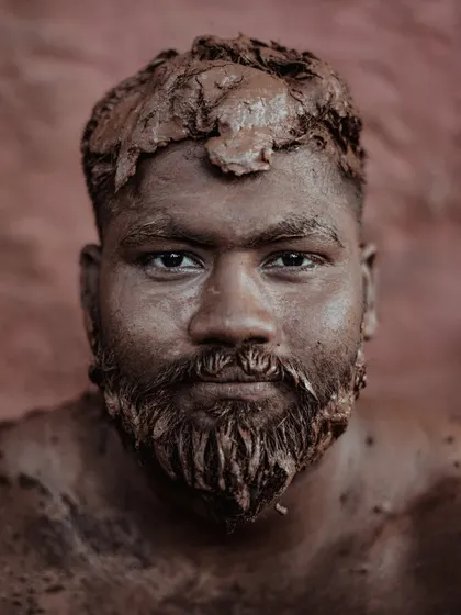 A portrait of a Kushti wrestler from Kolhapur, his face and body covered in the sacred mud of the 'taleem'. His direct gaze speaks of the immense strength, discipline, and tradition inherent in this ancient form of Indian wrestling.