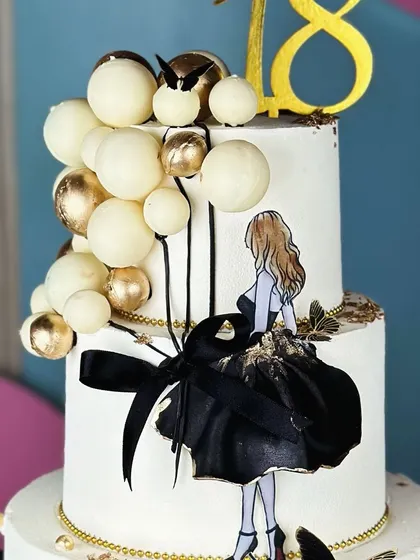 Understated luxury. This minimalist white, black, and golden cake for an 18th birthday is a masterpiece of simplicity and elegance, featuring a chic silhouette and balloon accents.