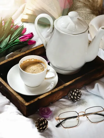 A wider view of the coffee in bed scene, showing the full tray with the teapot, flowers, and glasses. This lifestyle shot creates a complete and aspirational story.