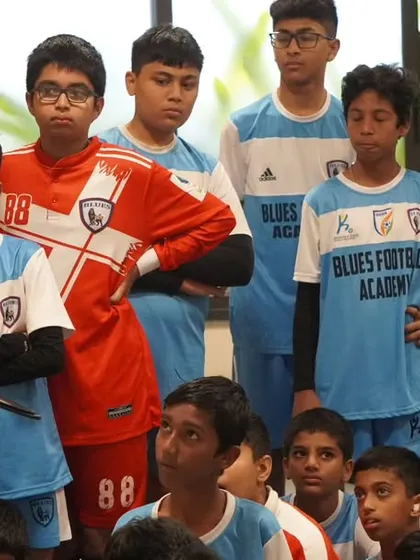 A group of players, including a goalkeeper, listen intently to their coach's tactical breakdown.
