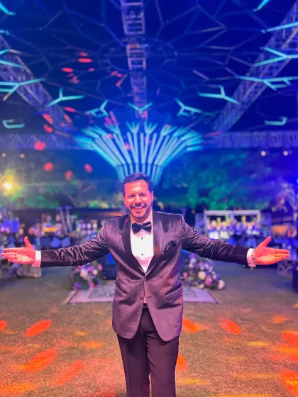 Arms open wide, welcoming everyone to a night of fun at a beautifully decorated outdoor Sangeet venue.