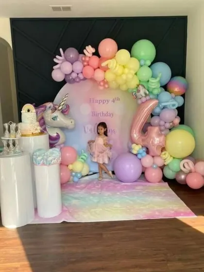 A dreamy unicorn-themed birthday setup with a pastel rainbow balloon garland and a backdrop featuring the birthday girl's name.