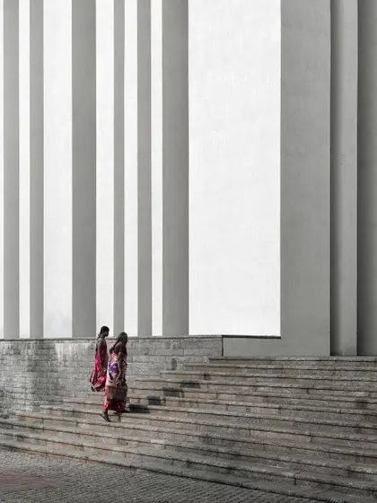 Where humanity and architecture converge. This photograph captures two women ascending the steps of the Sona University Centre, their colorful attire contrasting with the rhythmic white columns, telling a story of our shared journey.