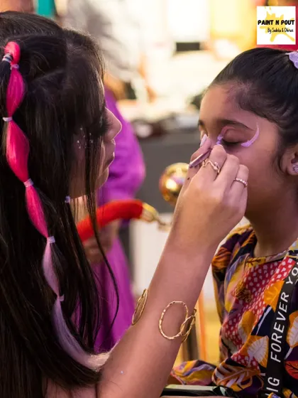 An artist carefully applies a whimsical design around a child's eyes. You can see the fun, temporary pink hair color in the background, another of our popular services.