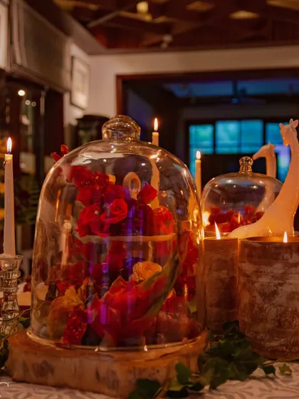 A glass cloche covers an arrangement of red dragon fruit and flowers, creating a beautiful still-life composition. This technique protects delicate items while turning them into a focal point.