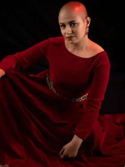 A dramatic shot in a rich, red velvet gown. The makeup is kept elegant and understated to complement the vibrant color of the dress and the model's confident pose.