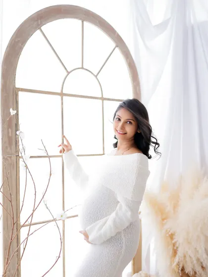 A serene portrait by the window. The mom-to-be is dressed in a cozy white knit dress, bathed in beautiful, soft natural light.