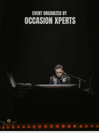 An atmospheric shot of A.R. Rahman at his piano, with the event organizer's name credited. A simple yet powerful image from the concert.