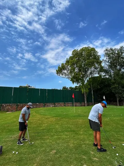 Two friends work on their chipping and pitching on our real turf short game area under a beautiful blue sky.