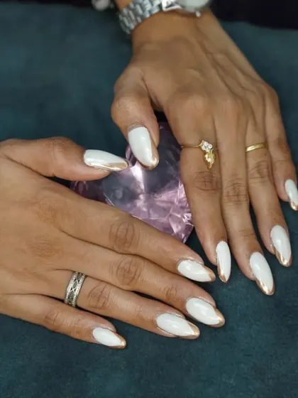 A clean and elegant look featuring almond-shaped nails with a crisp white base and a striking gold chrome edge. This is a popular choice for a sophisticated and polished style.