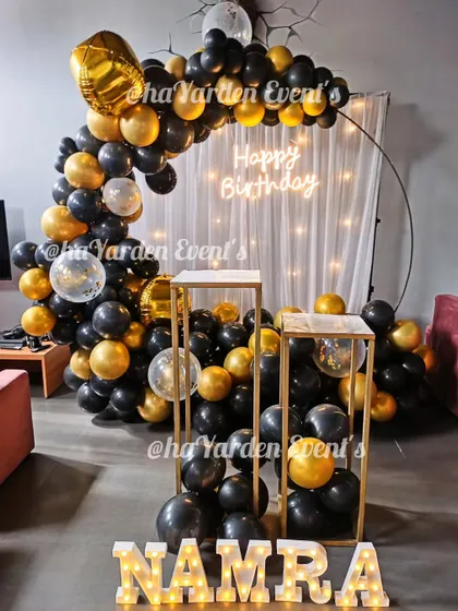 A chic black and gold half-ring balloon setup. The fairy light curtain and marquee letters add a touch of glamour to this home celebration.