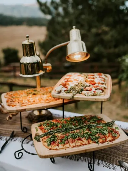 A rustic outdoor pizza station setup. I use tiered stands and heat lamps to serve different kinds of freshly baked pizzas, keeping them warm and ready for guests.