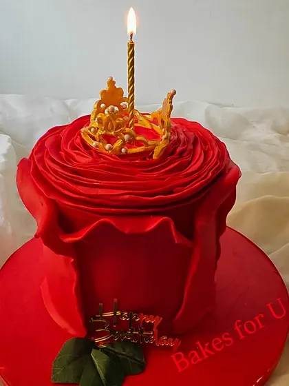 A stunning sculpted cake designed to look like a blooming red rose. The delicate petals are crafted from fondant, and a single lit candle emerges from the center.