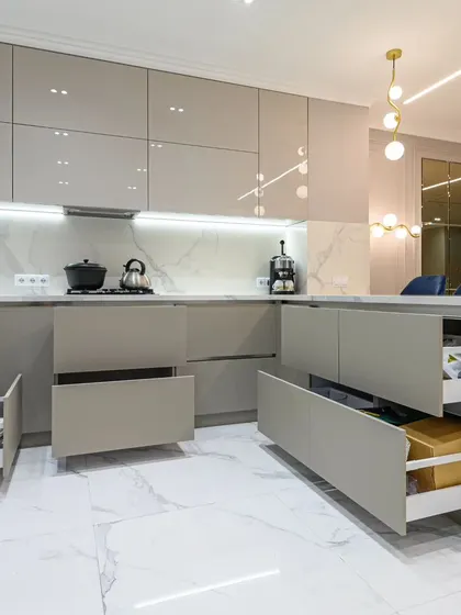 This image showcases the extensive storage in our minimalist studio flat kitchen. Multiple deep drawers in the island and along the wall provide ample space for pots, pans, and groceries, all concealed behind a sleek, handle-less facade for a clean aesthetic.