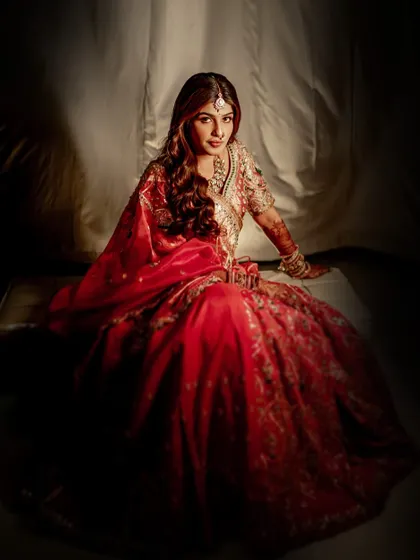 A full-length portrait creating a sense of drama and royalty. The rich red of her lehenga and the soft glow of her makeup create a truly memorable image.