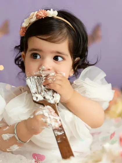 A close-up shot of a baby girl tasting frosting off a wooden prop during her whimsical cake smash.