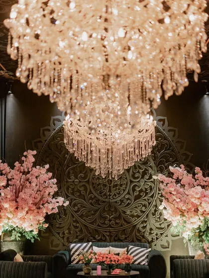A beautiful seating area with a dark green sofa set against a wall with a large, carved medallion. The space is framed by pink cherry blossom trees and illuminated by a magnificent crystal chandelier.