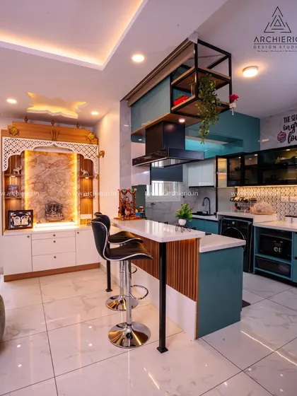 An open-plan layout where the kitchen, with its teal cabinets and breakfast bar, flows seamlessly into the living area, anchored by a beautiful pooja unit.
