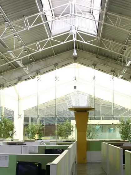 Inside a repurposed factory shed at TCS Yantra Park, where the industrial truss roof and skylights were retained to create a voluminous, day-lit workspace. This adaptive reuse project combines industrial heritage with modern office needs.