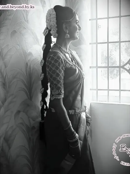 A black and white shot that captures the timeless elegance of a South Indian bride. This highlights the intricate details of the traditional jadai hairstyle and the beautiful silhouette of the draped saree.