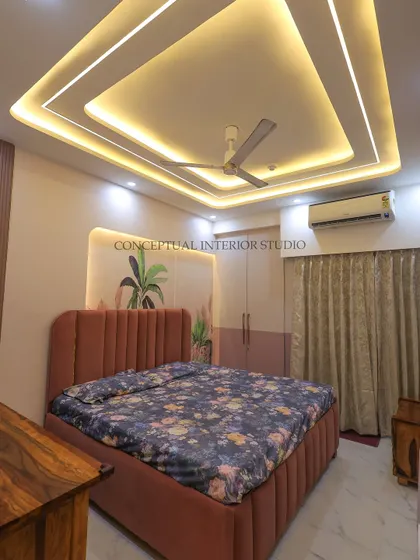 This bedroom showcases a modern look with a beautiful false ceiling design with cove lighting, creating a warm and inviting ambiance. The bed has a plush, fluted headboard.
