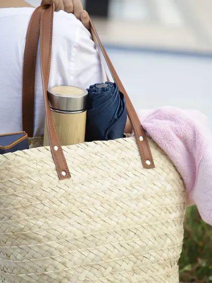 This lifestyle shot shows the practical elegance of our woven tote bag. It's spacious enough to carry all your essentials, from a bamboo water bottle and towel to a wallet and umbrella, making it the perfect companion for a day out.