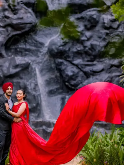 A beautiful couple portrait with a waterfall backdrop. The vibrant red of the gown stands out against the natural rock and greenery, creating a romantic and eye-catching anniversary photo.