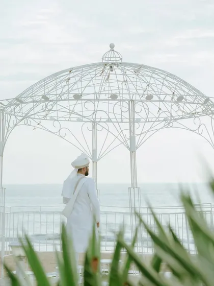 The groom stands by the sea, looking out at the horizon, a moment of calm before the ceremony.