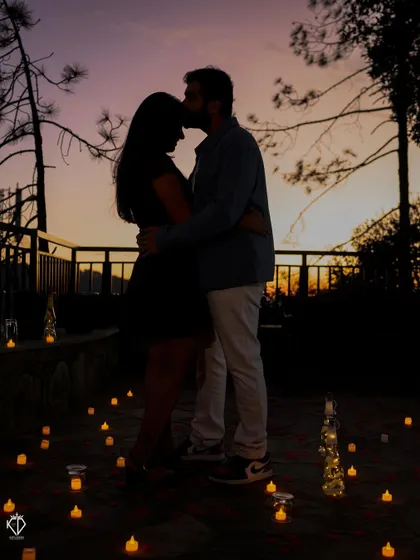 A tender silhouette of a forehead kiss, with the couple surrounded by the soft glow of candles and the fading light of dusk.