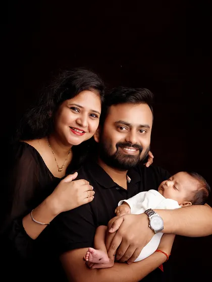 A proud new family of three. The parents' joyful smiles and the peacefully sleeping newborn create a perfect first family portrait.