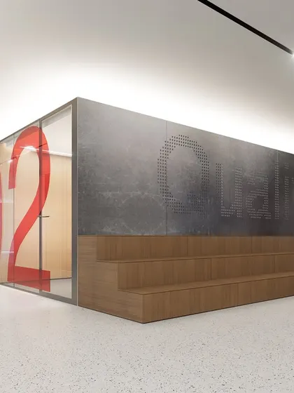 Tiered wooden seating provides an informal gathering spot within the Vian Office, adjacent to a glass-walled meeting room with bold graphics. This multi-functional space serves as a hub for presentations, team huddles, and social interaction, fostering a collaborative environment.