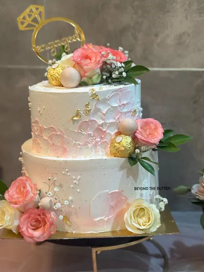 This two tier engagement cake combines modern texture with classic romance. I used a palette knife to create a subtle texture and decorated it with beautiful pink and white roses, Ferrero Rocher, and a touch of gold leaf.