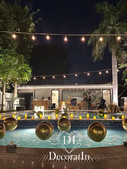 The poolside area of the 40th birthday bash, illuminated by string lights and dozens of floating candles and golden orbs in the pool. The setup includes a stylish bar area in the background, perfect for an evening of celebration.