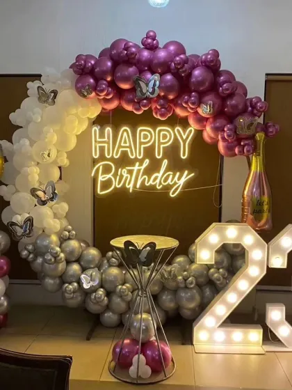 A glamorous 23rd birthday celebration featuring large light-up marquee numbers, a custom "Happy Birthday" neon sign, and a chic balloon arch in magenta, silver, and white with butterfly accents.