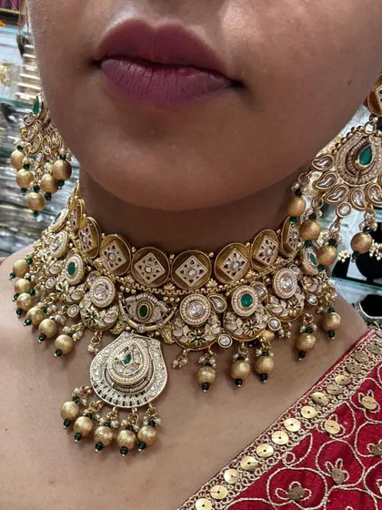 A close-up of a model wearing an antique-finish choker with intricate detailing and green stones, paired with a red embroidered outfit.