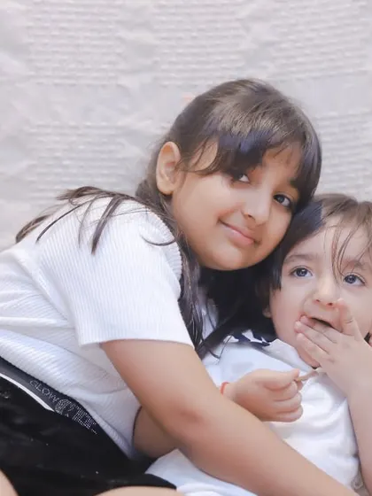 A candid moment on a comfy studio setup, with a big sister hugging her little brother who's enjoying a snack.