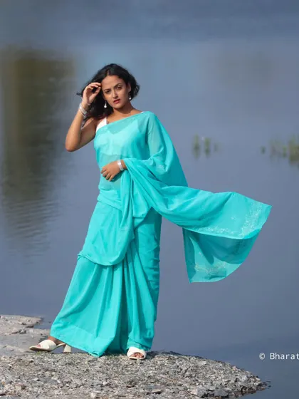A stunning outdoor portrait by the water. The flowing turquoise saree against the calm blue water creates a beautiful, ethereal image.