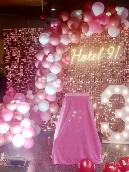 A 3rd-anniversary celebration for Hotel 91. The decor features a rose gold sequin wall, a pink balloon arch, and a marquee number '3'.