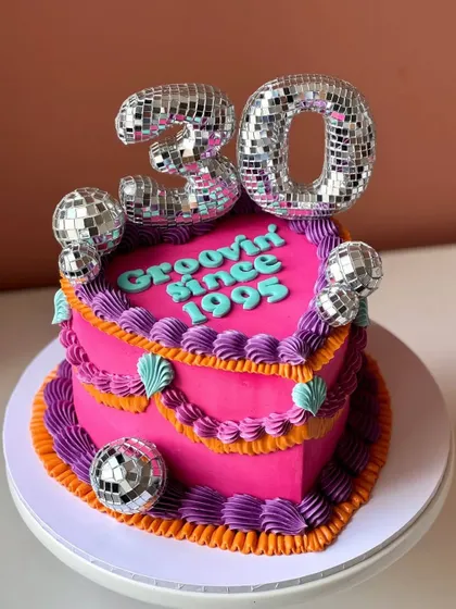 A groovy, heart-shaped disco-themed cake for a 30th birthday, complete with disco ball toppers.
