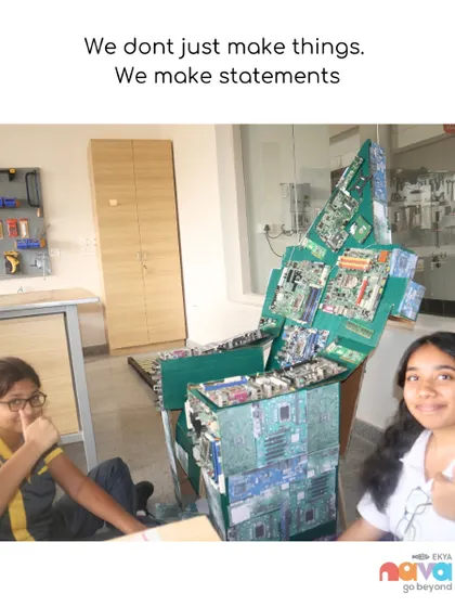 "We don't just make things. We make statements." Two students proudly present a chair they constructed from recycled electronic components, embodying our philosophy of design with purpose and environmental consciousness.