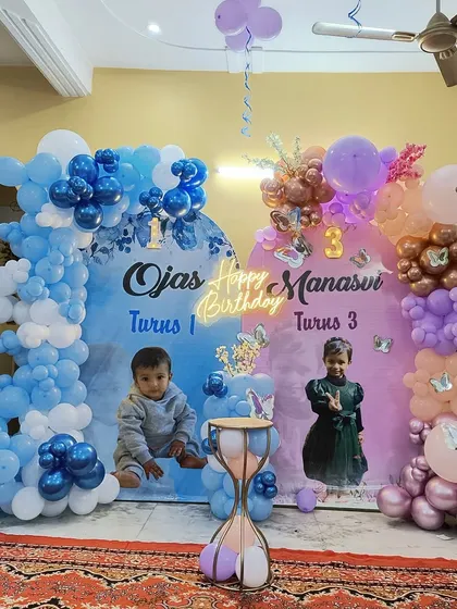 A combined birthday celebration for Ojas and Manasvi. This setup features two separate backdrops with their photos, framed by blue and pink balloon arches to give each child their own special space.
