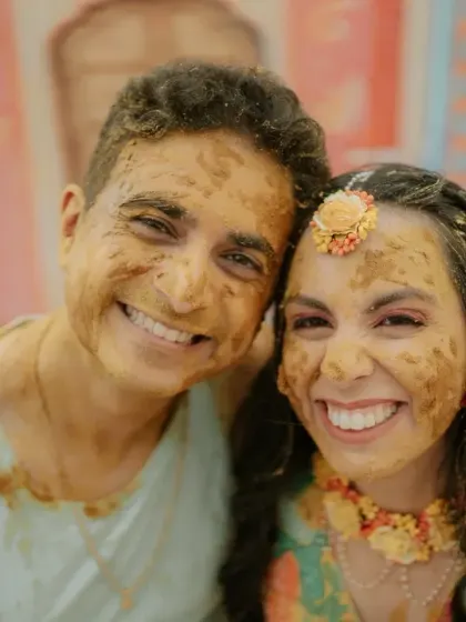 The happy couple smiling for the camera, their faces covered in turmeric paste during their fun and messy Haldi ceremony.