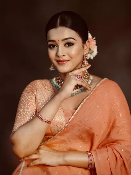 A portrait showcasing the complete look with the peach lehenga, including hair, makeup, and jewelry.