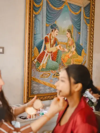 A behind-the-scenes look at the bride getting her makeup done, with a traditional painting of Radha and Krishna in the background. This frame beautifully connects modern preparations with timeless love stories.