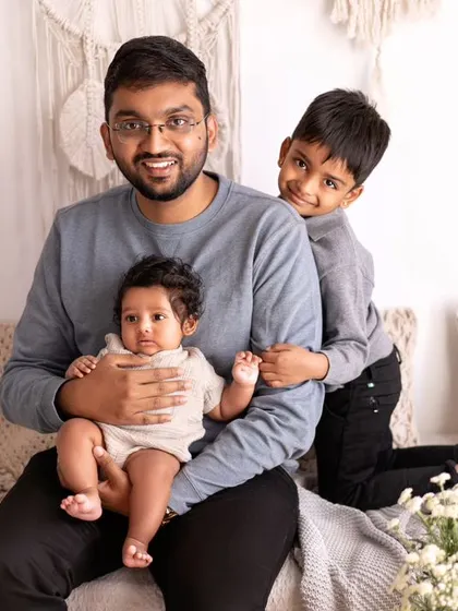 A father sits with his two sons. The older brother playfully peeks from behind, adding a fun and candid element to this portrait of brotherly love.