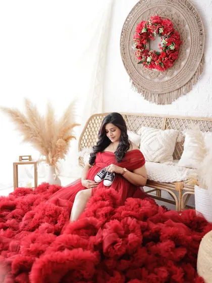 A sweet and symbolic portrait. The mom-to-be sits in a sea of red tulle, holding a tiny pair of baby shoes over her bump.
